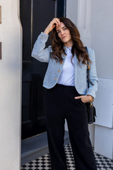 a lady in a blue tweed collarless jacket and a pair of black pants